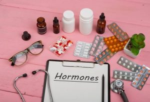 Assortment of pills, bottles, droppers, stethoscope, eyeglasses and a clipboard that says hormones, all for perimenopausal mental health
